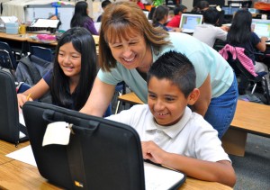 Le professeur a un rôle de tuteur et aide un élève sur un ordinateur lors d'une classe inversée